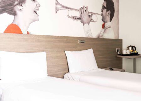 Modern hotel room with twin beds, stylish artwork, and in-room tea-making facilities, ideal for a comfortable stay.