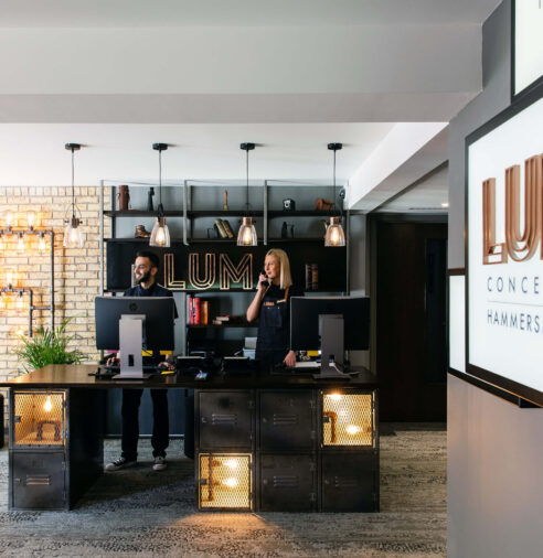 Stylish hotel reception with modern lighting, welcoming staff, and industrial decor in Hammersmith, London.