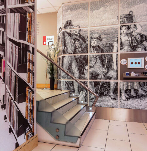 Stylish staircase in hotel lobby with vintage art, book-themed decor, and modern amenities for a welcoming experience.